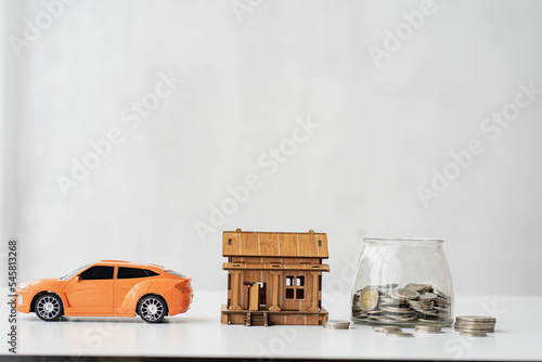 Piggy bank and toy car house on the table backdrop. white color concept of saving money for a house car
