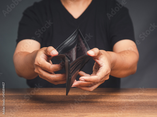 A young man opens an empty wallet while sitting at the table