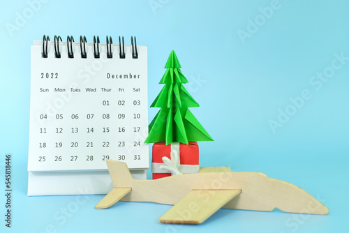 Selective focus of December 2022 desk calendar with airplane model and christmas tree on blue background. Christmas season vacation and holiday travel concept.