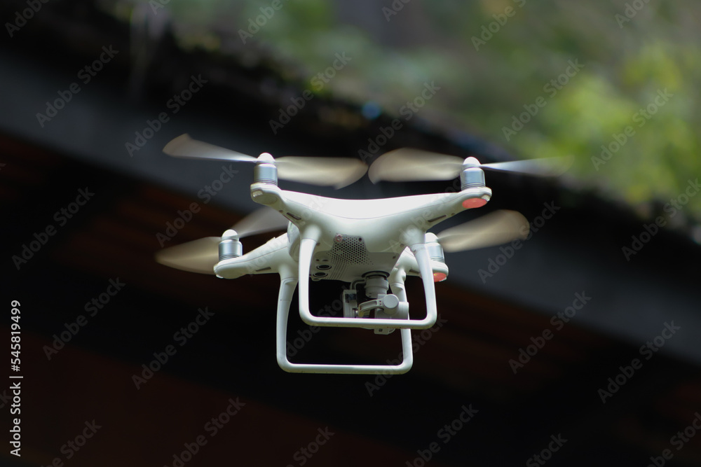 white drone flying between trees in forest white drone flying between trees in forest