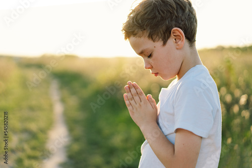 Boy closed her eyes and praying in a field at sunset. Hands folded in prayer concept for faith  spirituality and religion.