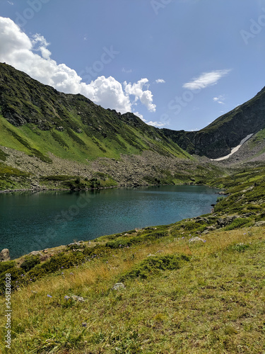 Beautiful view of the landscape of the Caucasus Mountains against a blue sky with clouds. View of the transparent Dukkinsky lake of emerald color. Vertical. Arkhyz, Karachay-Cherkessia, Russia