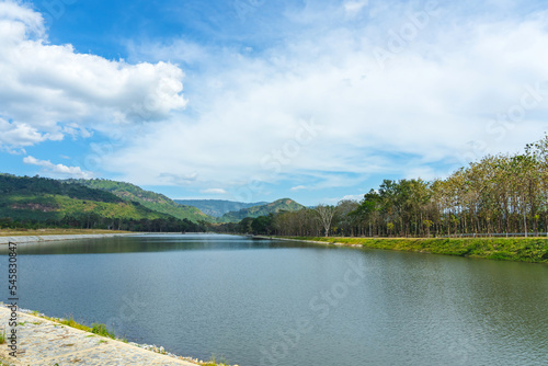 Fototapeta Naklejka Na Ścianę i Meble -  Beautiful and peaceful view of large reservoir with surrounding mountain and trees in beautiful sunshine and cloudy sky in Thailand. Tranquil and beautiful natural scenery landscape of reservoir lake.