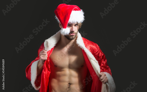 Christmas sexy man. Muscle man with bare torso at xmas. Santa with muscular body. Christmas party and sex games. Handsome sexy santa claus guy on black background. photo