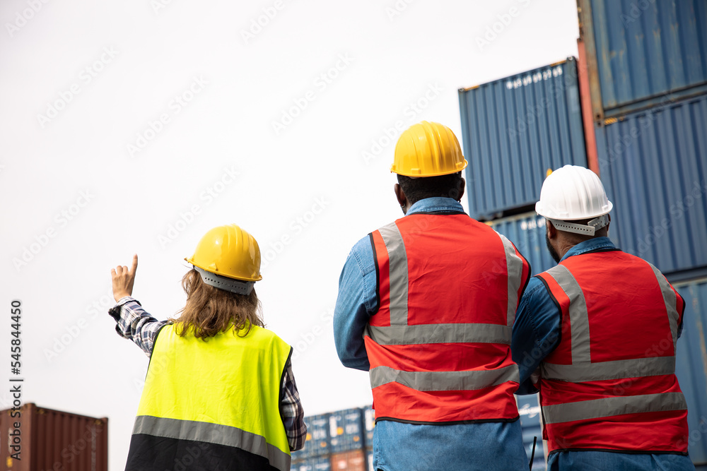 Back view of African American teamwork in safety jumpsuit with yellow helmet planing and talking at cargo container. Transport import,export logistic industrial Back view of African American teamwork in safety jumpsuit with yellow helmet planing and talking at cargo container. Transport import,export logistic industrial