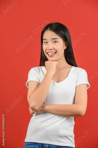 Portrait of Happy young asian woman in white t-shirt thinking creative person arm on chin isolated on red background