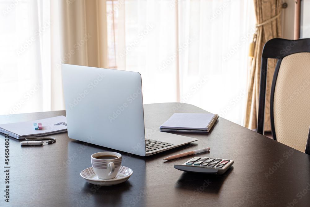 Close up of comfortable office desk with laptop, mug, tree, stationery and copy space on dark desk Close up of comfortable office desk with laptop, mug, tree, stationery and copy space on dark desk
