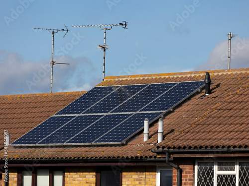 Roof on a house with solar panels and analogue TV aerials against blue sky