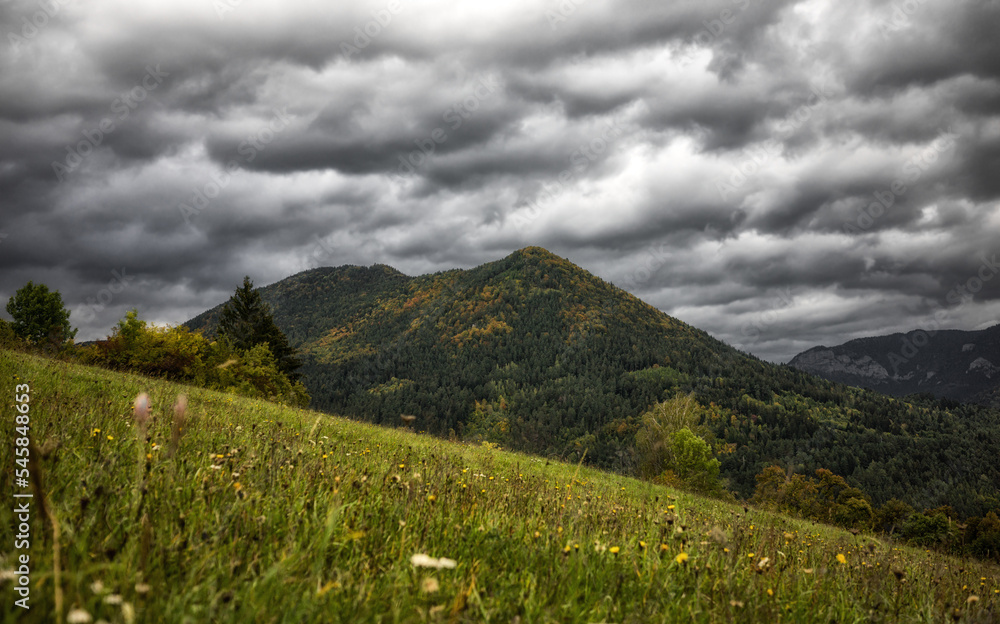 Stormy clouds on the sky over autumn country with meadow and hill at background