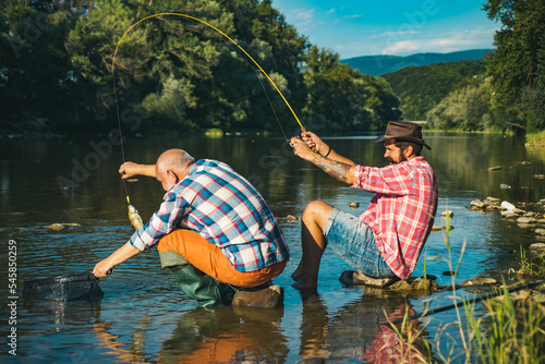 Young and old fisherman standing on the shore of lake with fishing rod. Father and son enjoy life. Men family, granddad and drandson fishing. Mature man fisher celebrate retirement.