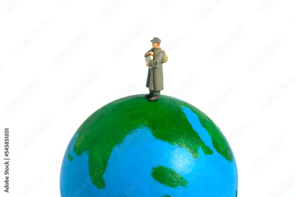 Miniature people figure toy conceptual photography. Global news delivery service A military mail officer holding news pack envelope standing above globe. Isolated on white background Miniature people figure toy conceptual photography. Global news delivery service A military mail officer holding news pack envelope standing above globe. Isolated on white background