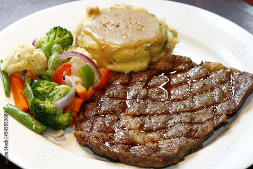 closeup of sirloin steak dish with assorted vegetables and gravied mashed potatoes