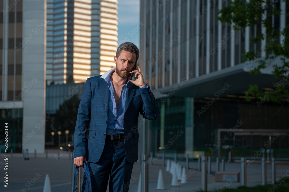 Portrait sexy businessman using smartphone near modern building outdoor. Successful business man walking in suit at street. Portrait sexy businessman using smartphone near modern building outdoor. Successful business man walking in suit at street.