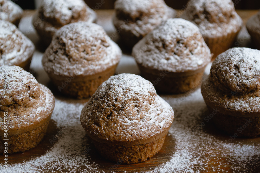 Close-up of delicious baked chocolate cupcakes on a wooden board and sprinkled with white powdered sugar Close-up of delicious baked chocolate cupcakes on a wooden board and sprinkled with white powdered sugar