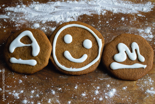 Three sweet cookies covered with white icing in the form of a smiley and the letters A and M lie on an old board surrounded by flour