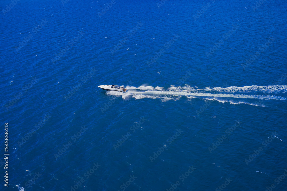 Obraz premium Speed boat in motion. Aerial view of a boat in motion on the water. Top view of the boat in motion. White boat fast movement on blue water.
