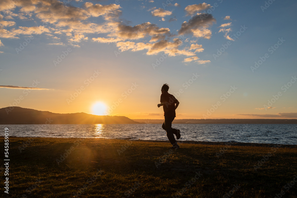 Silhouette image of a man running by Lake Rotorua at sunset, Rotorua, New Zealand.