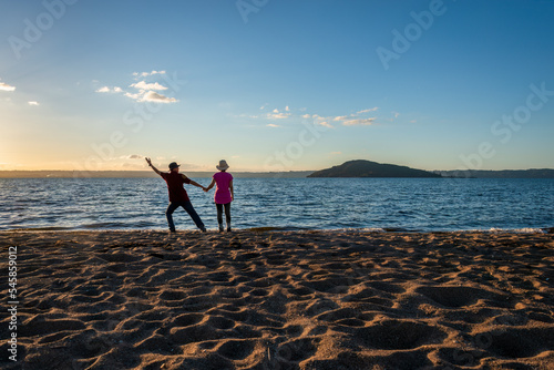 Tourists raising arm and enjoying lake Rotorua at sunset, Mokoia Island in the distance, Rotorua. photo