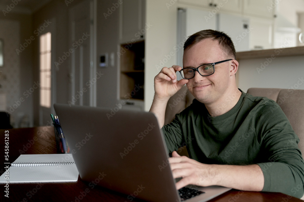 Cheerful adult man with down syndrome using laptop at home