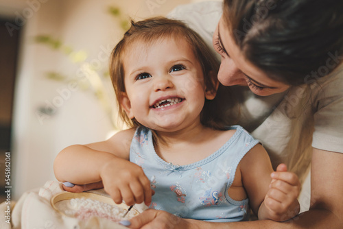 Mother sitting on the floor with her baby daughter and plays with threads while learning to knit. Needlework. Family leisure at home. People lifestyle. Fun