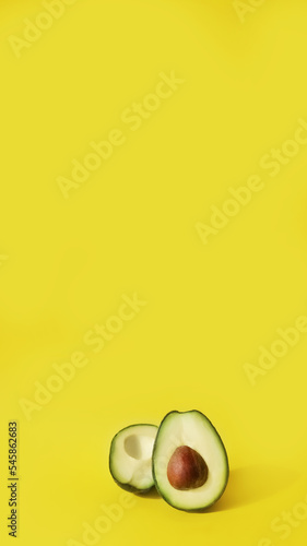 two halves of cut avocado fruit on yellow background, vertical, 16:9