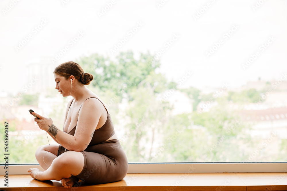 Ginger woman listening music and using cellphone after yoga practice