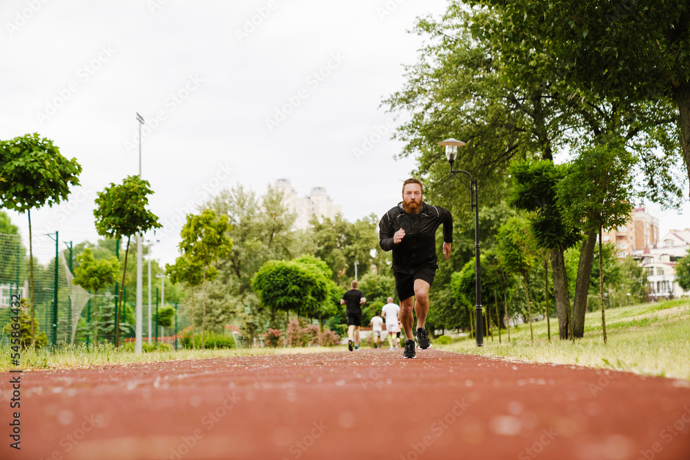 Portrait of adult bearded redhead man running on track