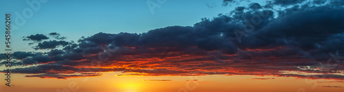 Setting sun painting red the bottom of a large gray cloud. Dramatic sky at golden hour. Bright vivid sunset sky panoramic shot. Picturesque wide skyscape at evening. Weather forecast. photo