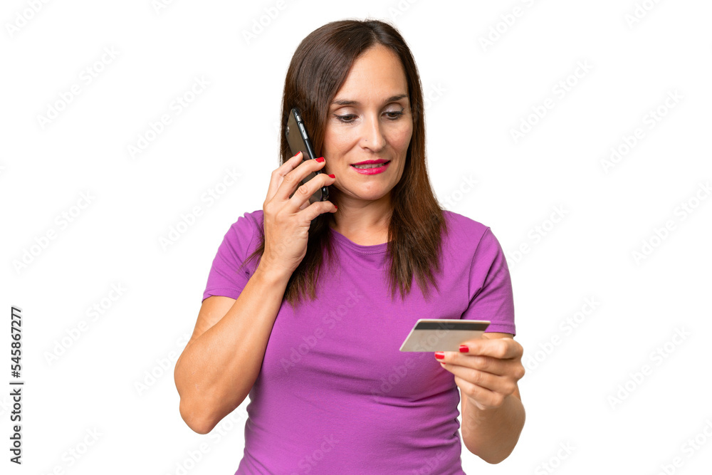 Middle-aged caucasian woman over isolated background buying with the mobile with a credit card Middle-aged caucasian woman over isolated background buying with the mobile with a credit card