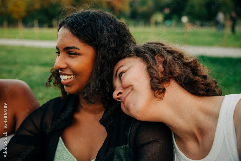 Smiling teenage girl leaning on friend's shoulder at park Smiling teenage girl leaning on friend's shoulder at park