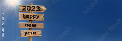 2023 happy new year writting on a wooden postsign on sunny blue sky photo