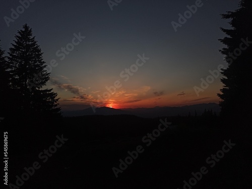 Sunset in the mountains  the last sun rays hiding behind a mountain peak.  Pine trees silhouettes and the fading day. Evening in the Carpathians  Carpathian mountains in Ukraine