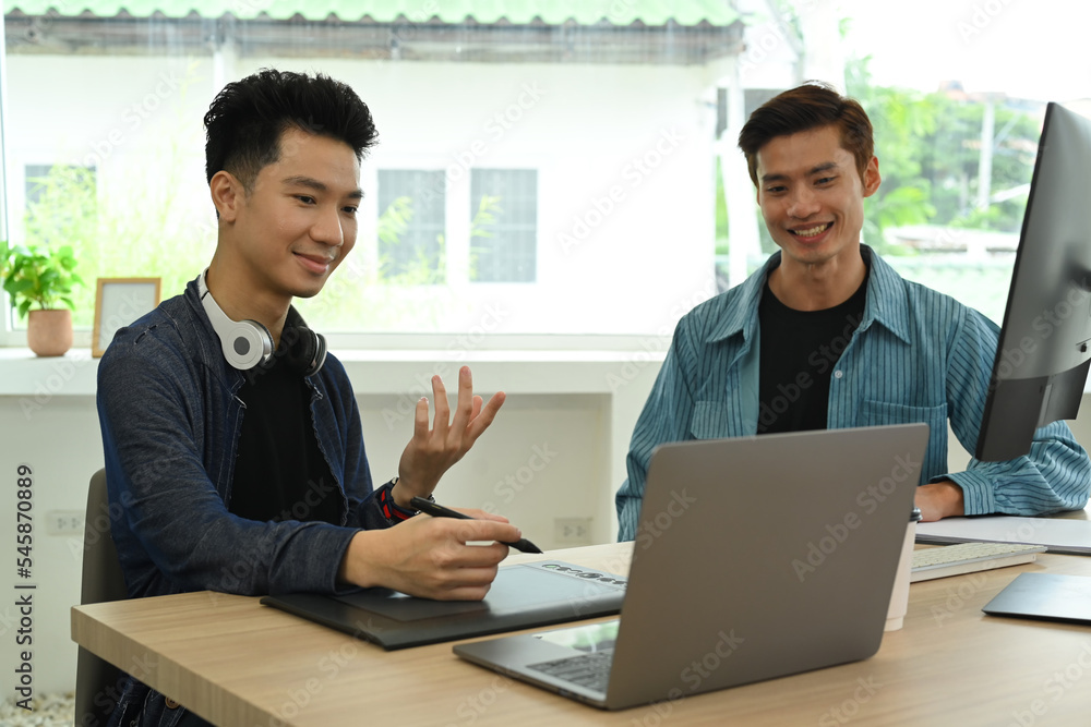 Two happy creative man looking at laptop screen and discussing online project at graphic studio Two happy creative man looking at laptop screen and discussing online project at graphic studio