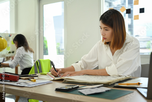 Concentrated Architects woman inspecting construction blueprints in modern office