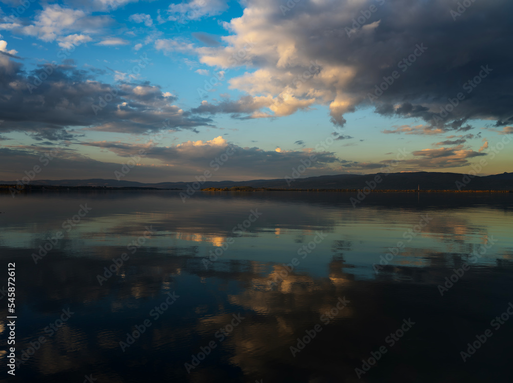 Bright beautiful Sunset landscape. Lake water surface with reflection of clouds in the water