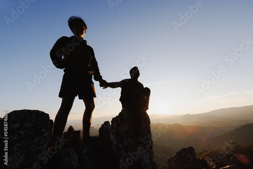 Silhouette of hiker helping each other hike up a mountain at sunset. People helping and, team work concept.