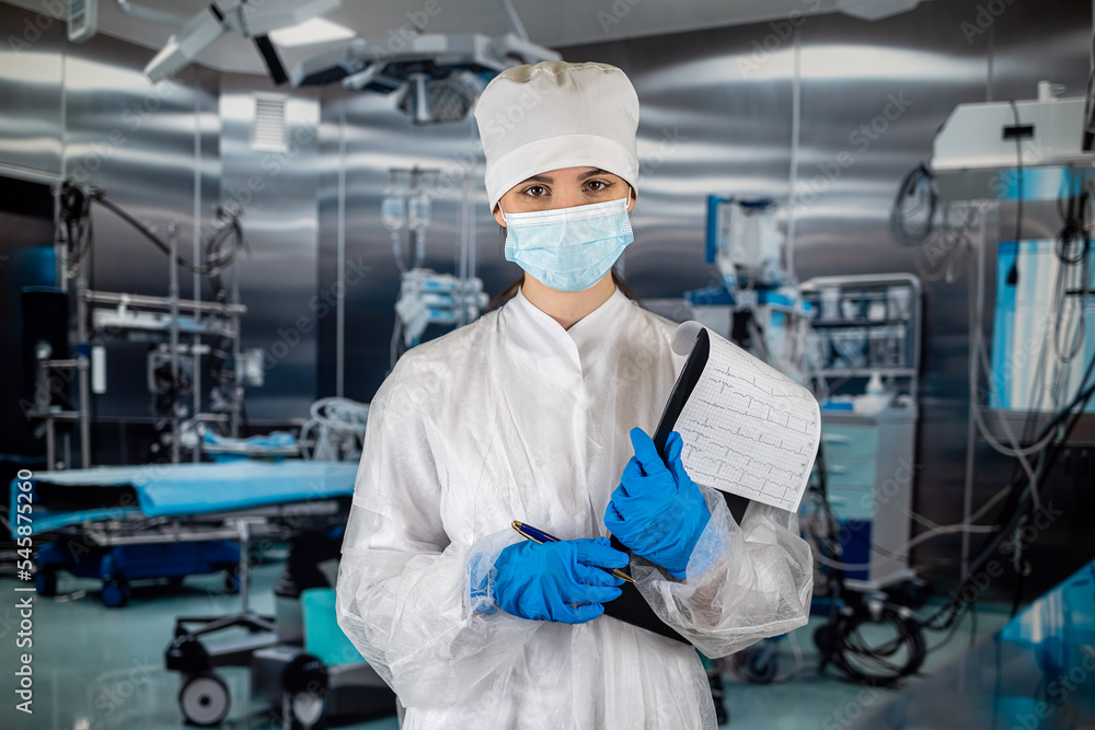 doctor with stethoscope in operating room holding clipboard with operating room in background. doctor with stethoscope in operating room holding clipboard with operating room in background.
