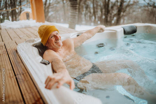 Senior man enjoying outdoor bathtub at terrace during cold winter day.