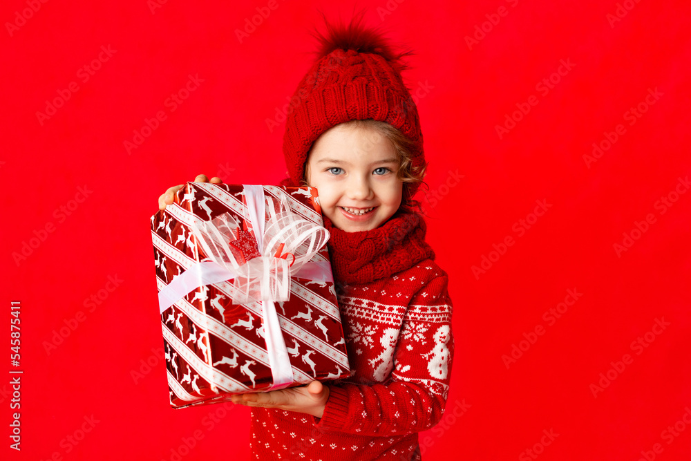 child a little girl in winter clothes holds a gift on a red background. New year's concept, space for text child a little girl in winter clothes holds a gift on a red background. New year's concept, space for text