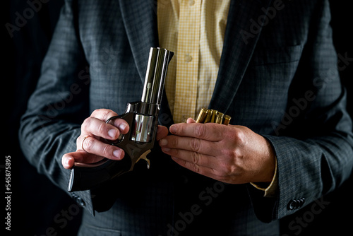 one male spy in a professional tuxedo holds a revolver pistol before the start of a film shoot. © RomanR