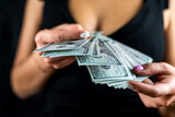 Cropped view of young sexy woman in black dress counting US dollar money in hands.