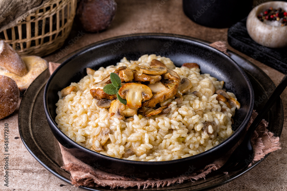 Risotto with porcini and champignon mushrooms in a black plate on brown background.