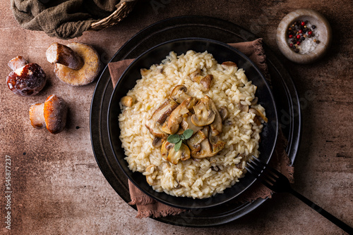 Risotto with porcini and champignon mushrooms in a black plate on brown background, directly above. photo