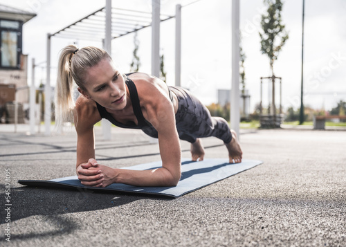 Young sportswoman practicing plank pose on exercise mat photo