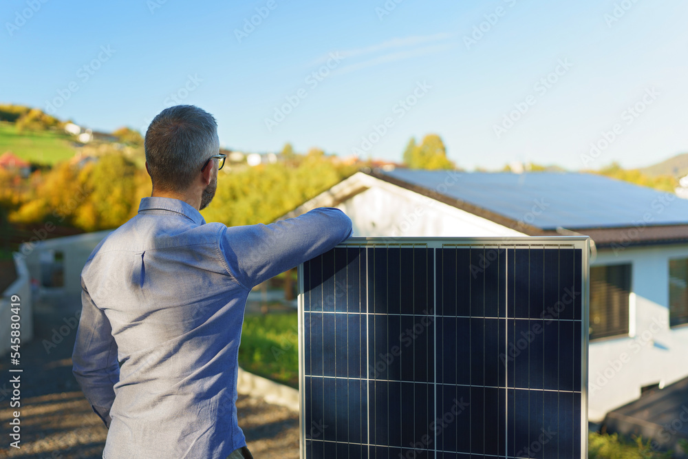 Happy owner holding solar panel, standing in front of his house.