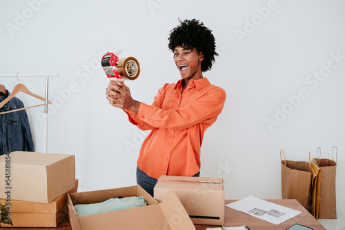 Cheerful young businesswoman with tape dispenser standing by desk photo