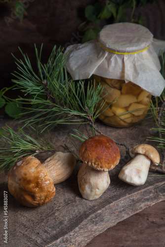 Three porcini mushrooms commonly known as Boletus Edulis and glass jar with canned mushrooms on vintage wooden background..
