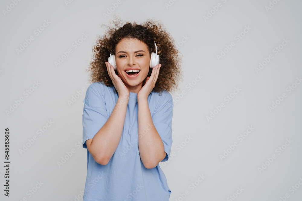 Young beautiful enthusiastic curly woman touching headphones looking at camera Young beautiful enthusiastic curly woman touching headphones looking at camera