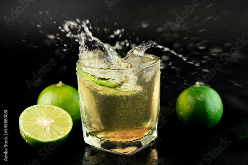 Shot of golden Mexican tequila with lime and salt on black background. A glass of tequila with lemon slices and splashing. Alcoholic drink concept. selective focus.
