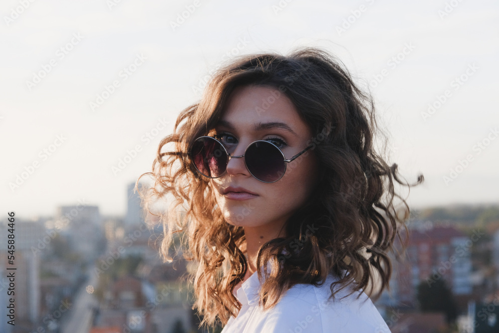 Attractive curly hair model in sunglasses at golden hour portrait.